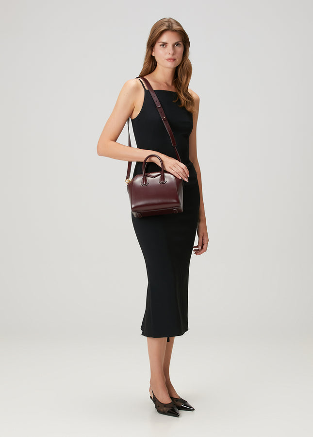Model wearing a burgundy Givenchy Mini Antigona leather bag over the shoulder with a black midi dress.